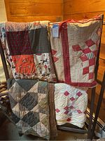 Four vintage quilts displayed on quilt rack showing varied patchwork styles and colors. Signs of aging visible.