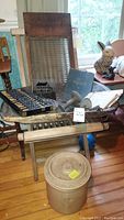Overview photo showing antique wooden washboard with glass, wooden dough bowl, abacus, scale hook, historical book, and school report cards arranged on a wooden chair in a room with wooden floor.