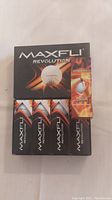 Photo shows five boxes of Maxfli Revolution golf balls arranged in a grid. Each box has clear branding with the Maxfli Revolution name and imagery including a golf ball and flame design.