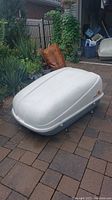 Side view of white Sears X-Cargo car-top luggage carrier showing curved lid and gray base on brick surface.