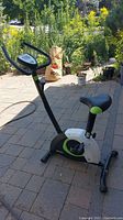 Side view of stationary exercise bike showing black and white frame with green accents and padded seat.