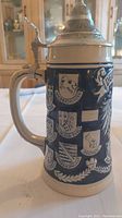 Side view of the stein showing multiple German city crests in relief on dark blue ceramic.