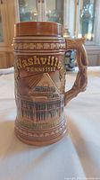 Left side view of brown ceramic beer mug with relief image and text reading 'Nashville Tennessee' and an image of The Grand Ole Opry House.