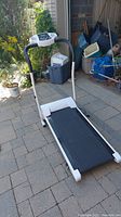 Full view of portable treadmill set up on a patio showing white and black design, running belt, handrails, and control console.