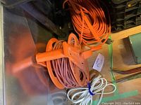 Photo of three extension cords including an orange cord on a reel, a coiled orange cord, and a white cord with a multi-outlet power strip at the bottom.