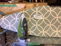 Black and Decker green and gray steam iron resting horizontally on ironing board, label with lot number visible.