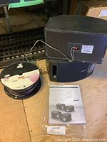 Pair of Bose 201 Series V black speakers, spool of 14 gauge RCA speaker wire, and Bose instruction manual on wooden floor.