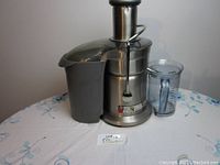 Side view of the stainless steel juicer with pulp container and juice jug on table.