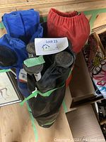 Three folding camp chairs in blue, red, and black fabric stored upright in their respective carrying bags tied with green straps.