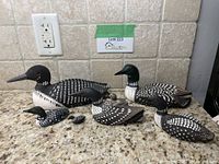 Full set of six carved and painted loon figurines arranged on granite countertop under tiled backsplash.