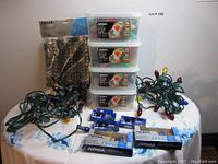 Full overview of lot showing multiple string lights, four plastic containers with NOMA Quick Clip LED light sets, replacement bulb packs, and quick clips on a cloth-covered table.