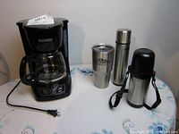 Photo of Black & Decker drip coffee maker with glass carafe and three stainless steel beverage containers on a table.