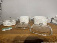 Front view of three CorningWare casseroles with lids on wooden surface showing matching pastel floral pattern