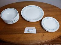Complete set of stacked dinner plates, side plates, and bowls arranged on wood table.