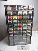 Front view of the black plastic organizer with small clear drawers filled with embroidery floss spools of various colors.
