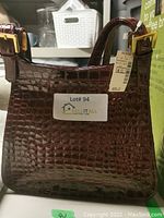 Front view of the brown crocodile pattern handbag with gold-tone buckles and original price tag attached.