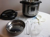 Instant Pot IP-DUO main unit with lid, inner pot, steaming rack, tongs, plastic spoons, and measuring cup arranged on table