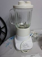 Full view of KitchenAid blender showing glass jar with measurement markings, white base with control buttons and power cord.