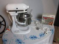 Wide view showing white mixer, stainless bowl, attachments and boxed food grinder