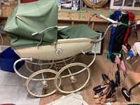 Side view of antique Silver Cross pram showing cream metal body and green fabric canopy with decorative floral emblem on the side.