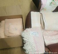 Five towels including peach bath towels with floral embroidery and fringe, cream and plaid towels in box and on chair