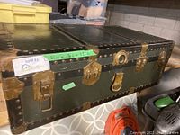 Full view of the vintage metal chest showing its rectangular shape, metal surface, metal studs and brass hardware details including the locking mechanism on the front.