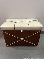Front view of vintage storage ottoman showing cream cushioned top with brown button details and brown base with cream trim.