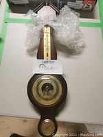 Full view of the weather station on a dark wood base with thermometer and barometer, partial wrapping visible.