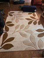 Full view of cream area rug with beige and brown leaf pattern on wood floor