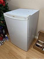 Photo of small white Kenmore bar fridge, exterior showing door, in a room on wooden floor.
