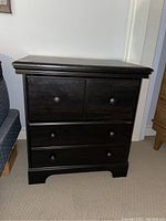 Front view of black wood bedside table showing upper two cabinet doors and lower two drawers with round black knobs.