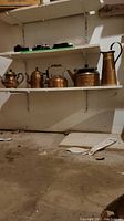Wide view of brass pots and pitcher on shelves in basement, showing overall condition and arrangement