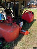 Red and orange marine gas tanks of various sizes and a bottle of chain saw oil placed on grass outdoors.