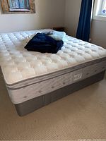 Queen size Serta Bruno mattress on gray box spring with folded navy comforter, green throw and white sheets on top
