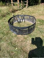 Photo showing entire round black metal fire pit with decorative cutouts of trees and deer, and several fire tools inside.