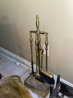 Fireplace tool set with four brass tools including brush, shovel, poker, and tongs on a brass stand