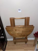 Folding table folded flat showing the semi-circular wooden tabletop and folding legs.
