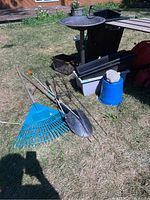 Overall view of garden tools, planters, blue urn, and bird bath arranged on grass.