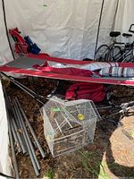 Full view of red and grey canvas hammock on black metal stand, with striped pillow, rolled fabric, and other outdoor items nearby.