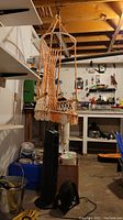 Hanging rope chair shown suspended in a basement workshop setting along with tower fan and desk fan visible on floor below.