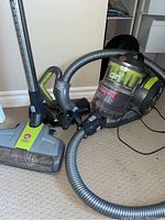 Full view of Hoover canister vacuum with visible hose, metal wand, and power nozzle attachment on carpet floor.
