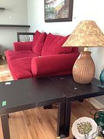 Two black square end tables placed side-by-side with a red couch and a lamp on one table. Tables have a laminate particle board top and screw-in legs.