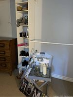 Photo showing white laundry basket, black handbag on shelving, umbrella, folding table with candles, some shoes on shelves
