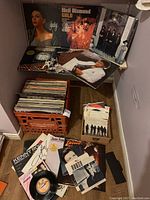 Shelf with four vinyl LP covers displayed above an orange milk crate filled with albums and a small box of singles.