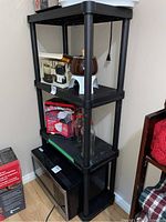 Full view of the black resin shelving unit with multiple shelves, an LG microwave on the bottom shelf, and miscellaneous contents on upper shelves (not included in sale).