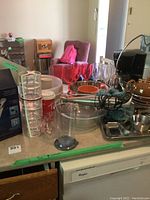 Overall kitchen counter showing various kitchen items including clear nesting glass bowls, Brown Betty tea pot, plastic wine glasses in red, and kitchen utensils.