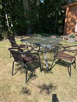 Full view of patio set with four chairs around square glass top table on grass in backyard.