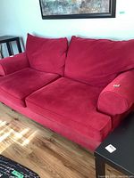 Full view of the red sofa showing seat cushions, back cushions, and one armrest with a small tag.