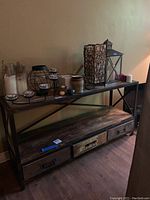 Full side view of the distressed metal and wood stand with three lower drawers and various decorative items on top.