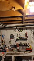 Wide view of basement workspace showing hand tools mounted on pegboard and scattered on workbench under exposed ceiling